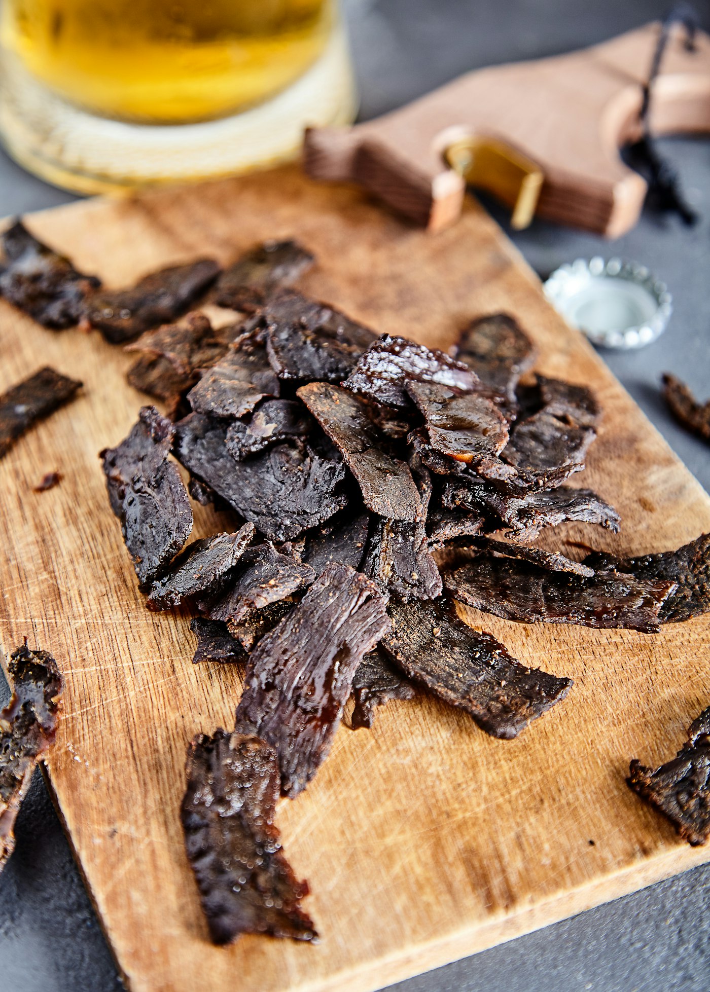 Strips of finished jerky, dark and dry with the grain showing, piled on a wooden board.