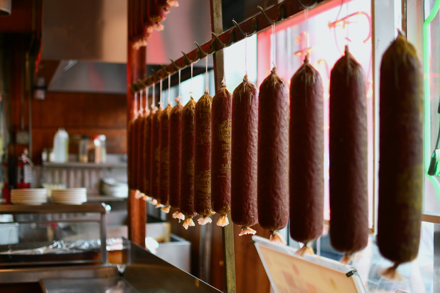 A rail of summer sausage chubs hanging in tied casings inside a shop.